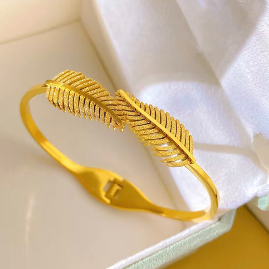 Open cuff / bangle featuring overlapping gold feather or leaf motifs with detailed texture work.